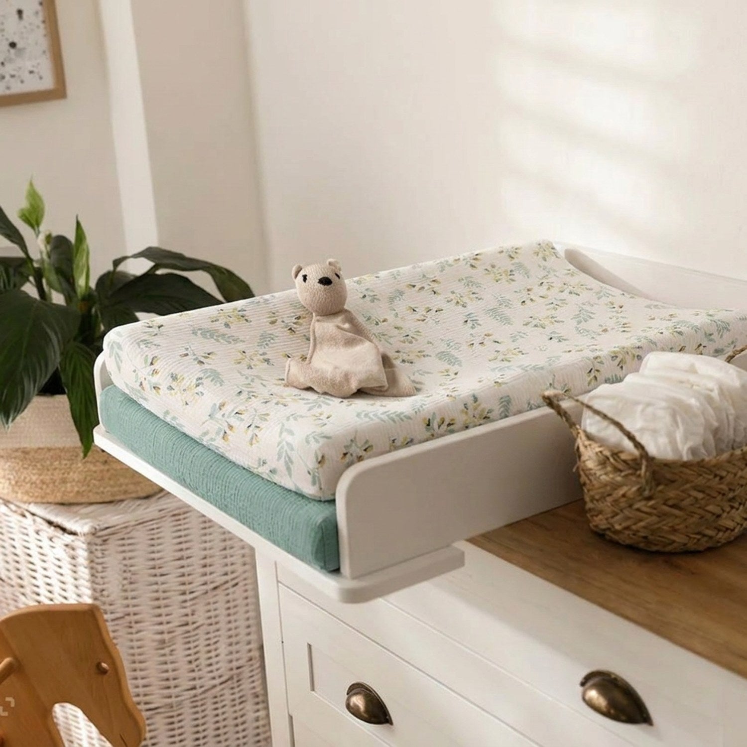 Housse de matelas à langer installée sur une table à langer avec un doudou et un panier de langes