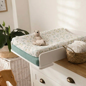 Housse de matelas à langer installée sur une table à langer avec un doudou et un panier de langes