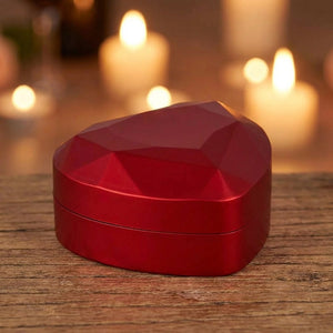 Boîte à bijoux rouge fermée en forme de cœur posée sur une table en bois aux chandelles