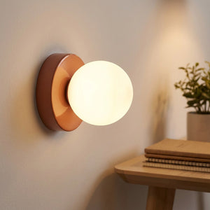 Applique murale terracotta allumée près d'un bureau avec plante et carnets