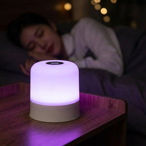 Lampe de chevet tactile allumée en violet dans une chambre sombre et cosy