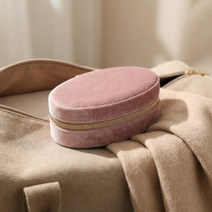 Boîte à bijoux en velours rose posée sur un sac de voyage