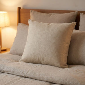 Housse de coussin beige posée sur un lit contre une tête de lit en bois avec une lampe de chevet