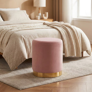 Tabouret rond en velours rose posé au pied d'un lit dans une chambre douce