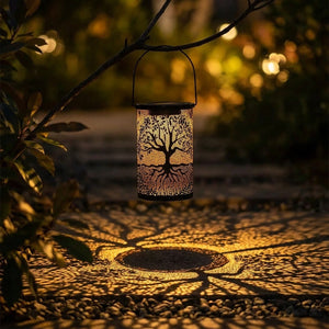 Lanterne solaire arbre de vie suspendue à une branche au-dessus d'une allée de jardin la nuit