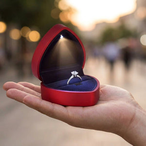 Boîte à bijoux rouge ouverte tenue dans une main avec une bague et lumière LED