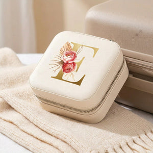 Boîte à bijoux de voyage crème posée près d une valise sur un plaid