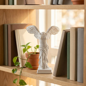 Statue de la déesse ailée en résine blanche sur une étagère à livres lumineuse