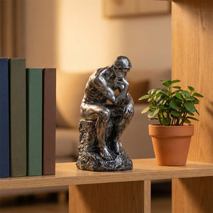 Statue Le Penseur de Rodin argentée posée sur une étagère avec une plante verte