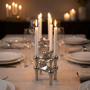 Chandeliers modulaires argentés alignés au centre d'une table de dîner aux bougies allumées