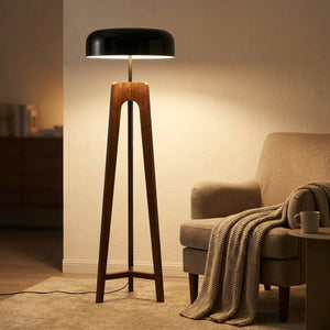 lampadaire trépied en bois foncé allumé à côté d'un fauteuil confortable et d'un plaid