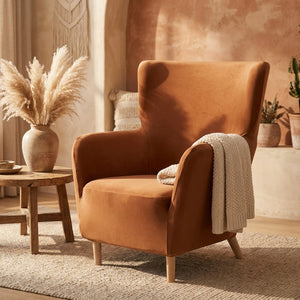 Fauteuil à oreilles en velours terracotta dans un salon bohème chaleureux avec pampa