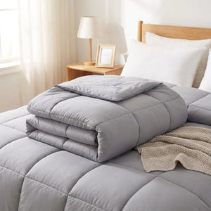 Couette moelleuse grise pliée sur un lit avec un plaid beige