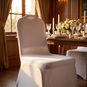 Chaise habillée de blanc en gros plan devant une table dressée avec bougies dans une salle à manger chaleureuse
