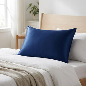 Taie d'oreiller en soie bleu marine posée sur un lit scandinave en bois clair