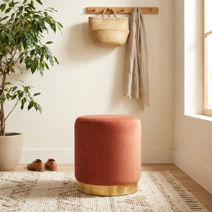 Tabouret rond en velours terracotta dans une entrée avec plante et tapis