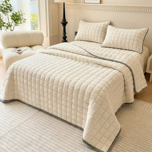 Couvre-lit matelassé velours écru sur un lit dans une chambre neutre avec fauteuil douillet
