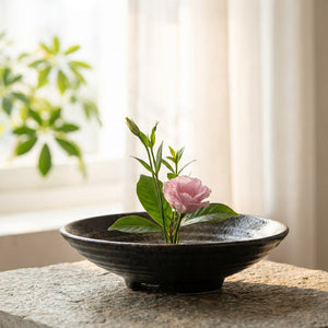Gros plan d'un vase ikebana en céramique noire près d'une fenêtre lumineuse