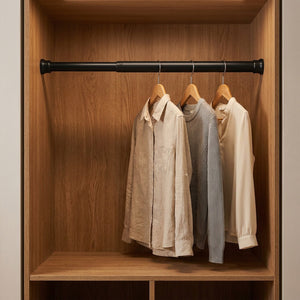 Tringle noire dans un dressing tenant des vêtements sur cintres en bois