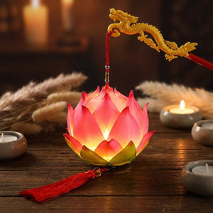 Lanterne lotus rose illuminée sur une table en bois entourée de bougies et de pampa
