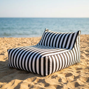 Pouf géant à rayures posé sur le sable d'une plage face à la mer