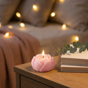Bougie parfumée en forme de rose allumée sur une table de chevet cosy