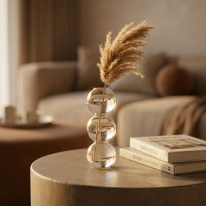 Vase en verre à bulles avec une tige de pampa sur une table en lumière dorée