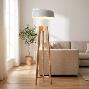 lampadaire trépied en bois clair au dôme blanc allumé dans un salon lumineux et végétal