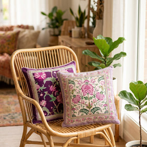 Deux housses de coussin florales bohème posées sur un fauteuil en rotin près d'une fenêtre avec des plantes vertes