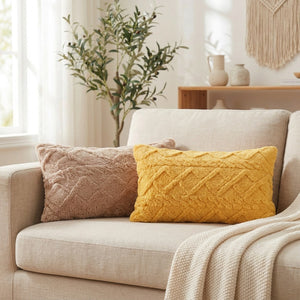 Housse de coussin lombaire en peluche posée sur un canapé en lin beige avec un plaid dans un salon chaleureux