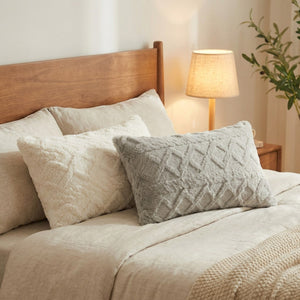 Coussin lombaire en peluche moelleuse installé sur un lit contre une tête de lit en bois avec lampe de chevet