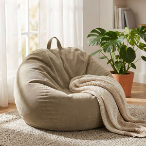 Pouf poire beige en velours côtelé dans un coin lecture avec plaid et plante