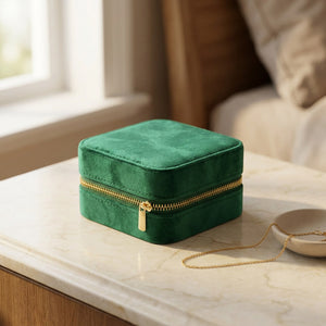 Boîte à bijoux en velours vert émeraude fermée posée sur une coiffeuse avec un collier doré