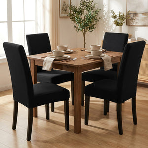 Salle à manger avec quatre chaises habillées de housses noires autour d'une table en bois