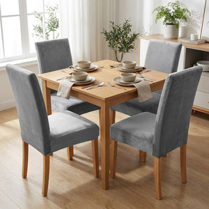 Salle à manger avec quatre chaises habillées de housses grises en velours autour d'une table en bois