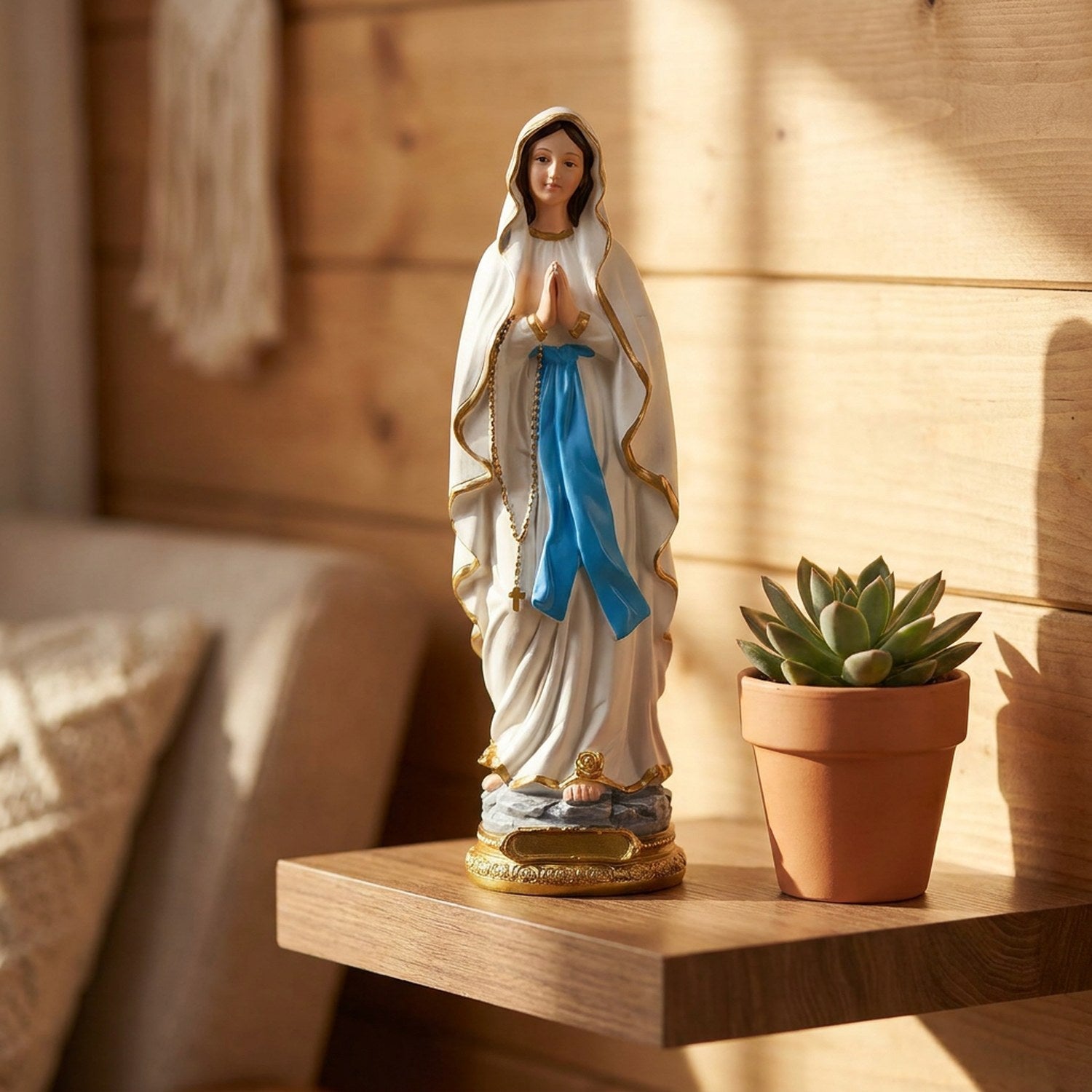 Statue de la Vierge Marie en résine sur étagère en bois avec plante verte en pot terre cuite lumière chaleureuse