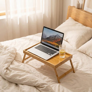 Plateau bambou pliable avec ordinateur portable ouvert sur lit blanc