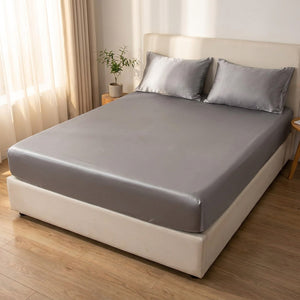 Drap housse gris en soie installé sur un grand lit avec une plante verte