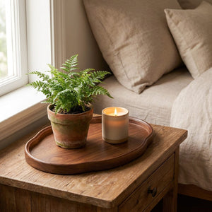 Plateau décoratif bois noyer avec fougère et bougie allumée sur table de chevet chambre cosy