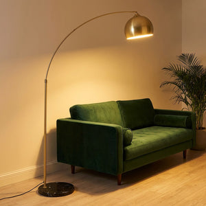 Lampadaire arc doré près d'un canapé velours vert en salon contemporain