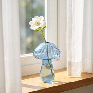Vase champignon en verre bleu sur rebord de fenêtre avec lumière naturelle