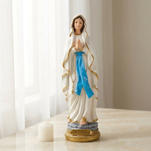 Figurine Vierge Marie résine blanche sur surface marbre crème bougie blanche près d'une fenêtre voilage blanc lumière naturelle