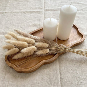 Plateau bois organique avec herbes séchées et bougie blanche sur nappe de lin beige