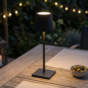 Lampe LED tactile noire allumée sur une table de terrasse en bois