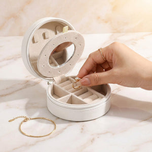 Coffret à bijoux de voyage blanc ouvert sur marbre avec main posant une bague
