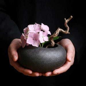 Mains tenant un vase céramique ikebana gris mat avec hortensias roses
