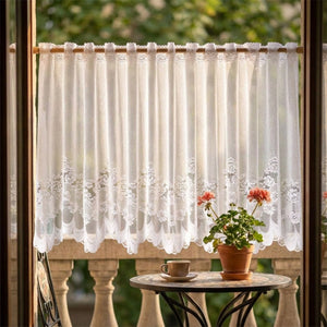 Rideau brise vue en dentelle sur un balcon avec table et geranium