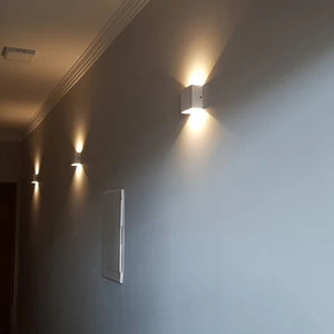 Suite d'appliques murales LED blanches éclairant un couloir d'entrée le soir