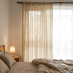 Chambre cocooning avec rideau en lin beige devant la fenêtre au petit matin