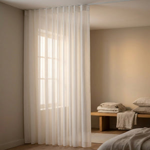 Rideau voile blanc dans une chambre cosy avec linge de lit plié sur un banc en bois
